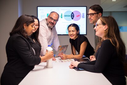 Six Colgate-Palmolive employees in a meeting room discussing a product concept, with a presentation slide on a screen behind them.